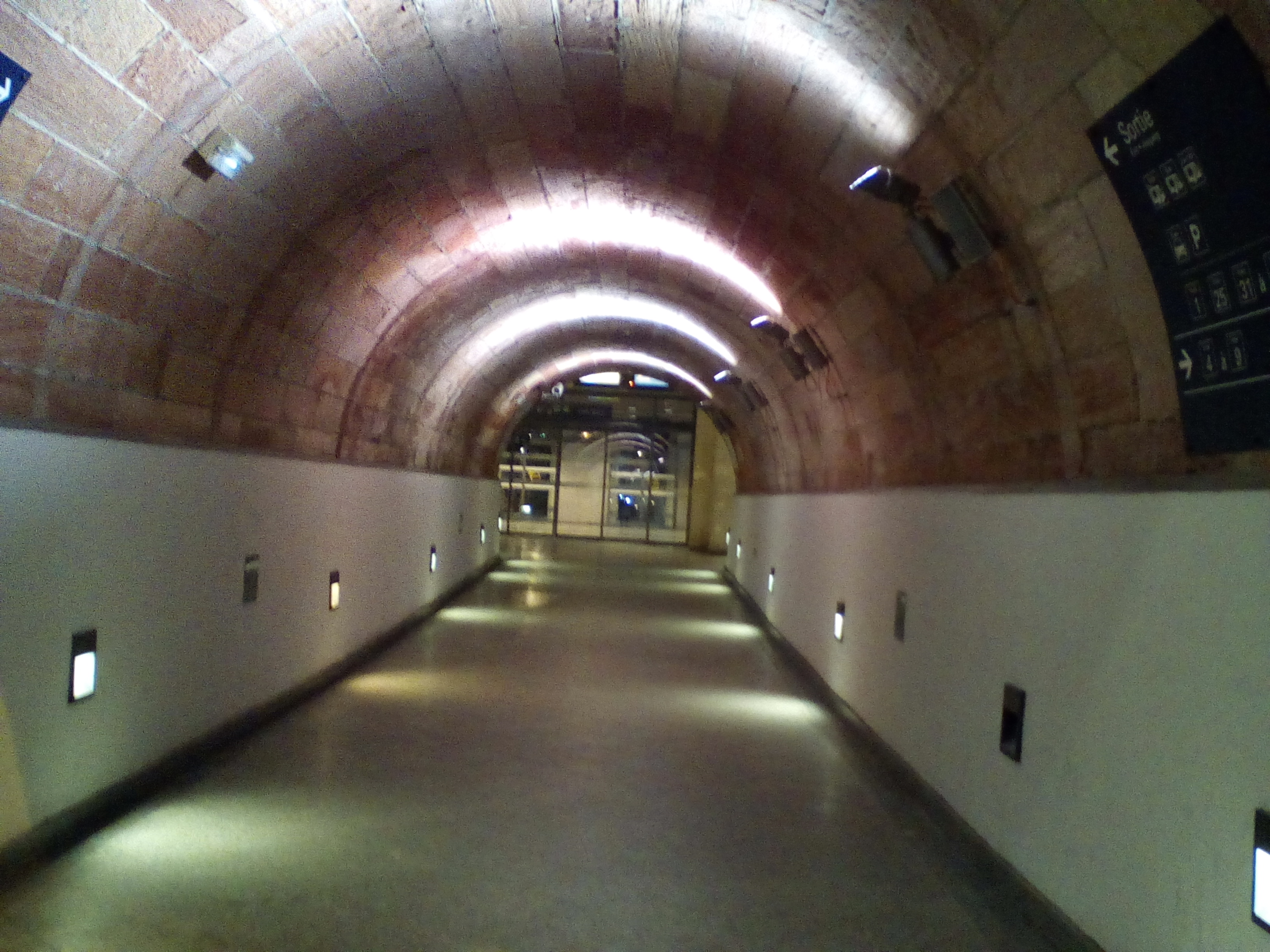 Tunel faiblement illuminé. La voute est arrondie, les murs sont blancs en bas et rougeâtres en haut.