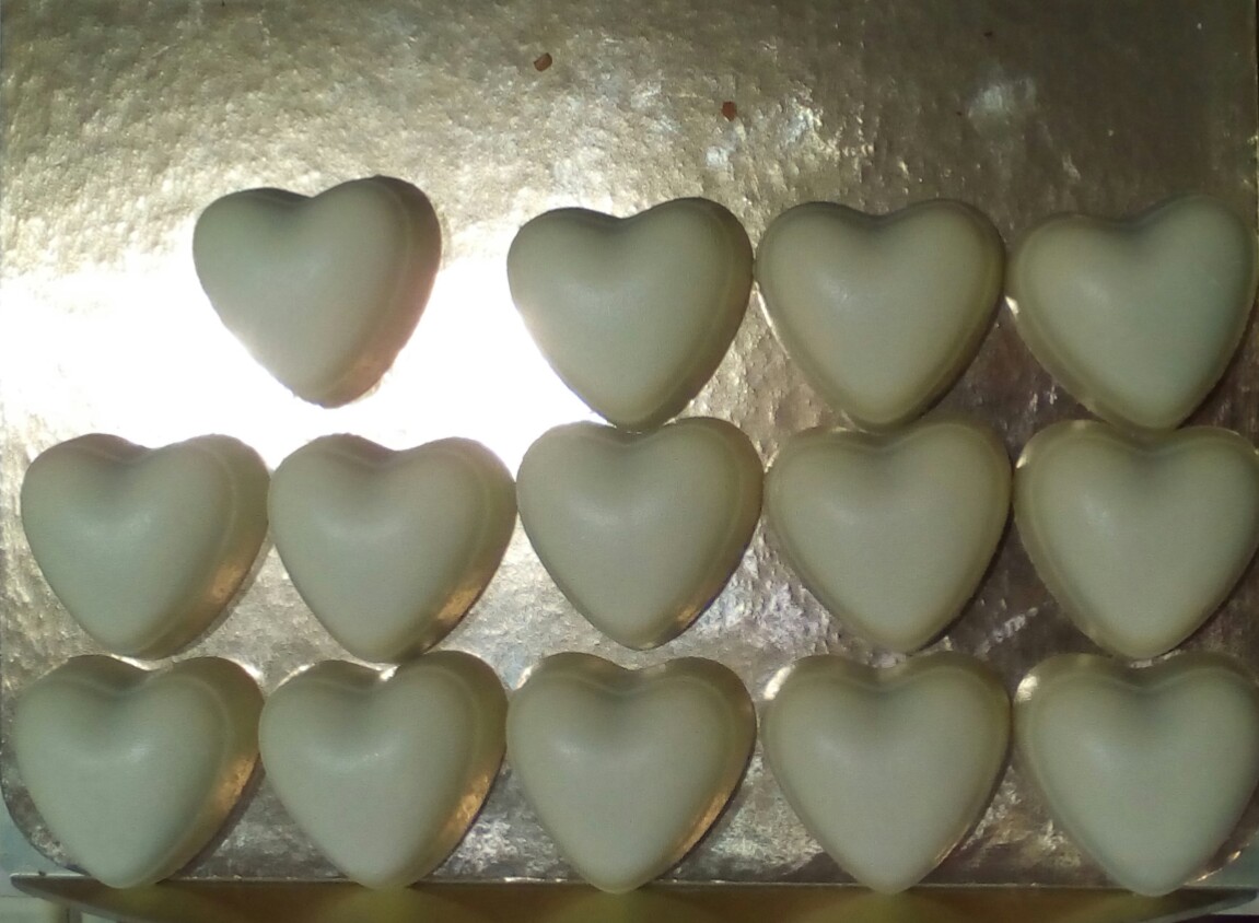 14 cœurs en chocolat blancs alignés en trois rangs sur du papier doré. Sauf le premier, qui n'est pas aligné.